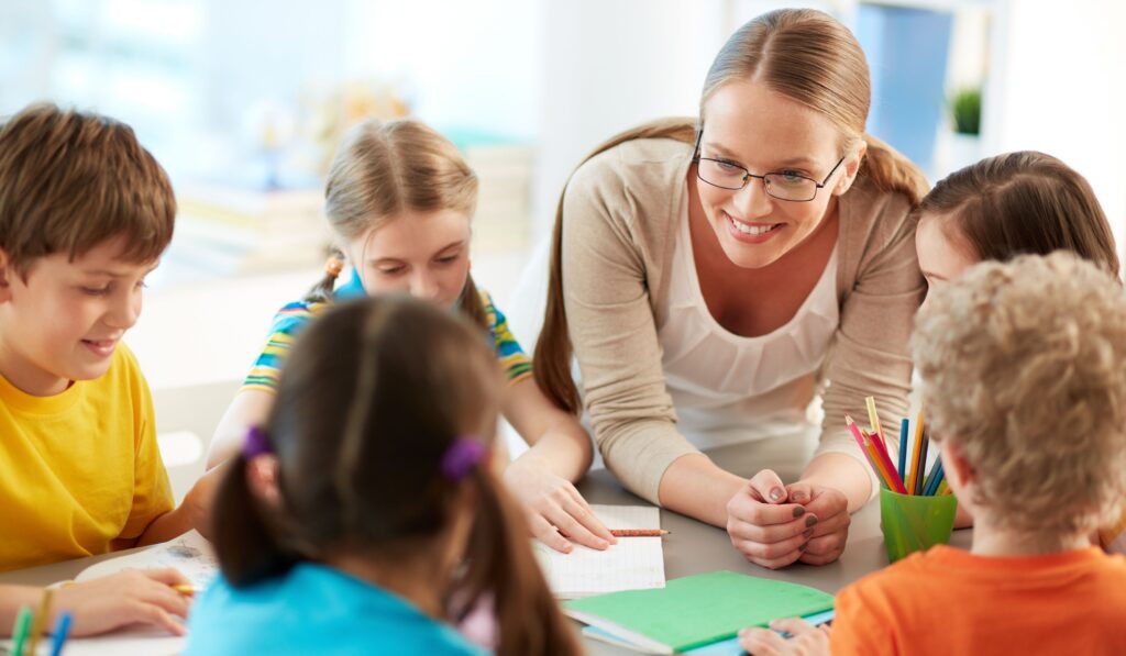 Image shows a happy teacher engaged with a group of young students