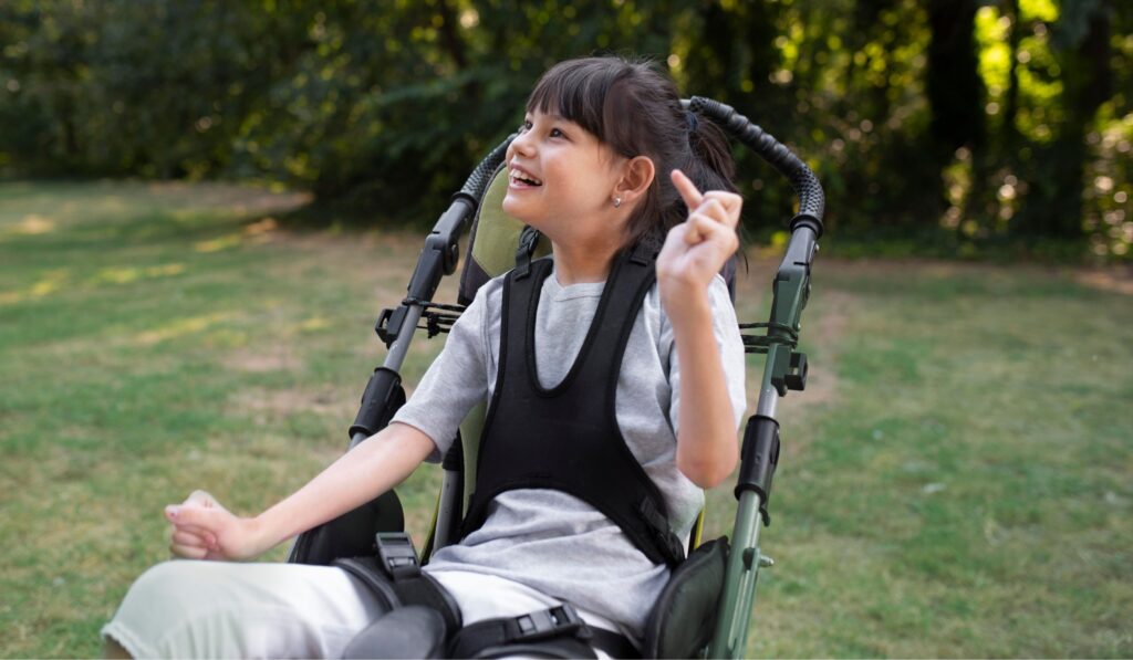 Photo shows a young girl in a wheelchair outside