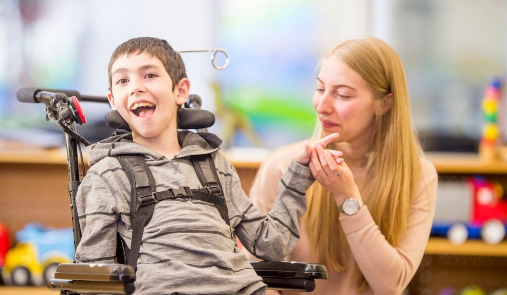 Image shows a young boy in a wheelchair with a therapist