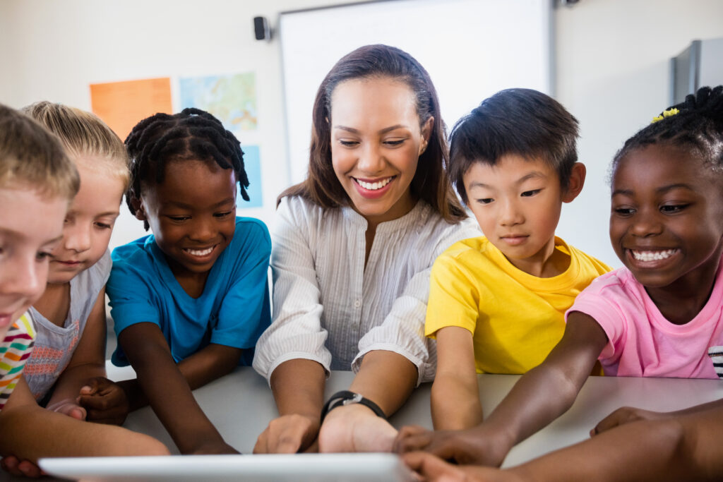 Image shows a young teacher with a group of diverse children using a tablet