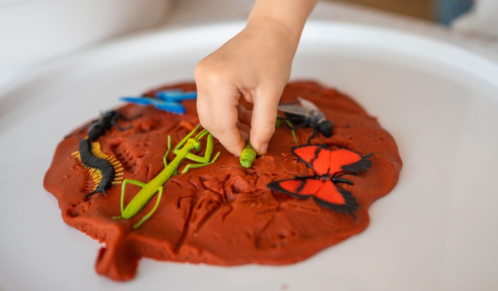 Image shows a child pushing plastic bugs into playdough "mud"