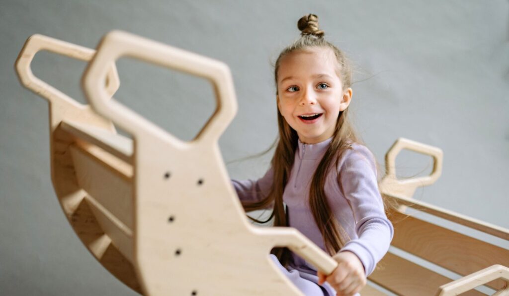 A young girl rocking in a wooden toy boat