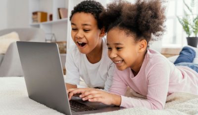 Two children are smiling and using a laptop together