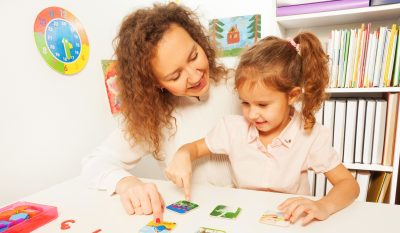 A therapist is helping a child select pictures on a table.