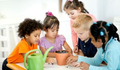 Image shows a group of young children planting a seed in a flower pot