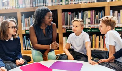 Image shows a young woman at a table in a library with three students